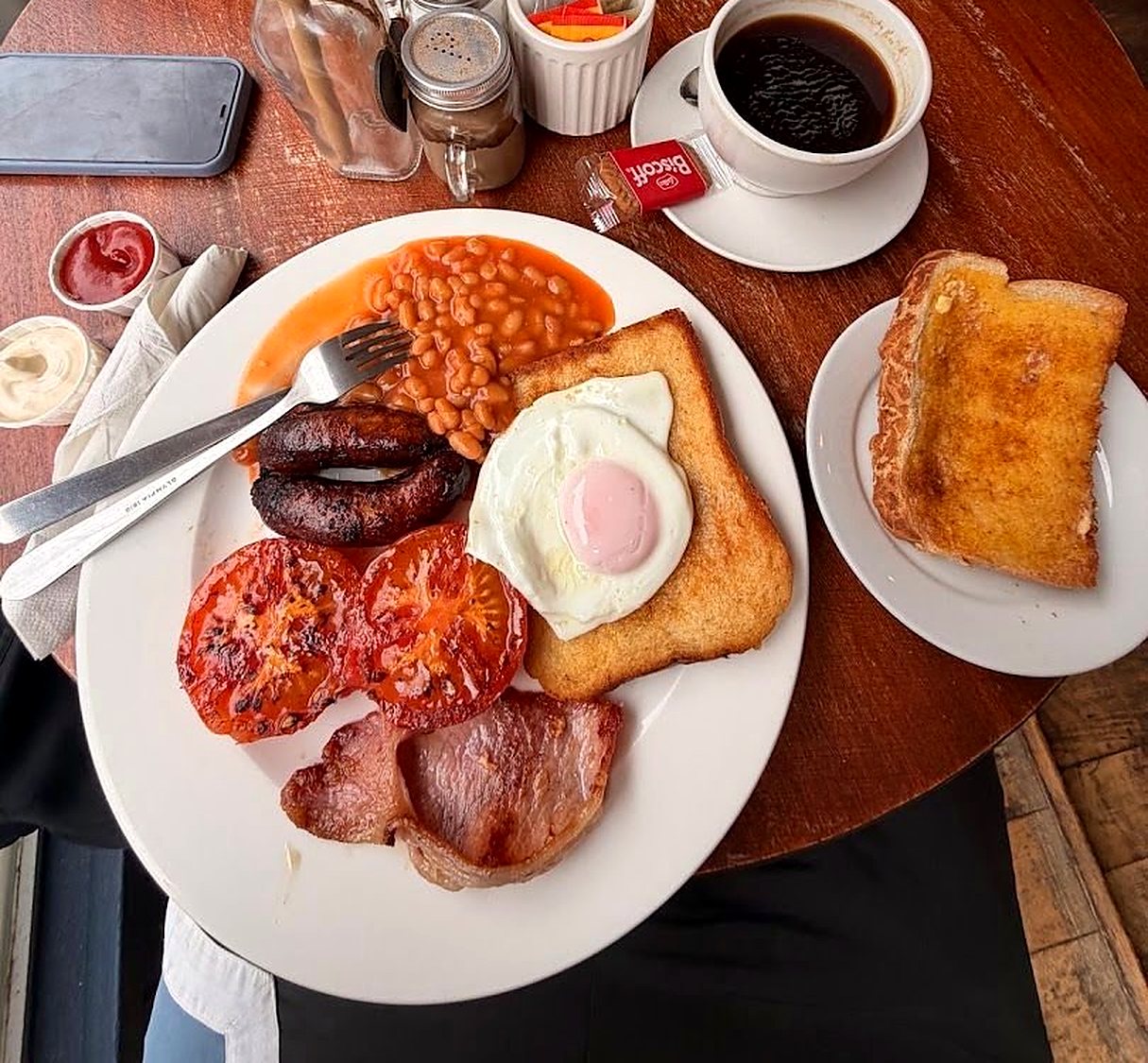 A full English breakfast: bacon, egg on fried bread, beans, sausages, black pudding and grilled tomatoes, with toast and black coffee